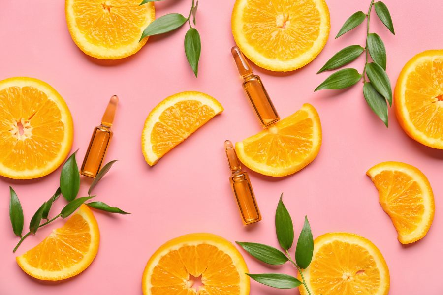 naranja y ampollas de vitamina C en fondo rosa
